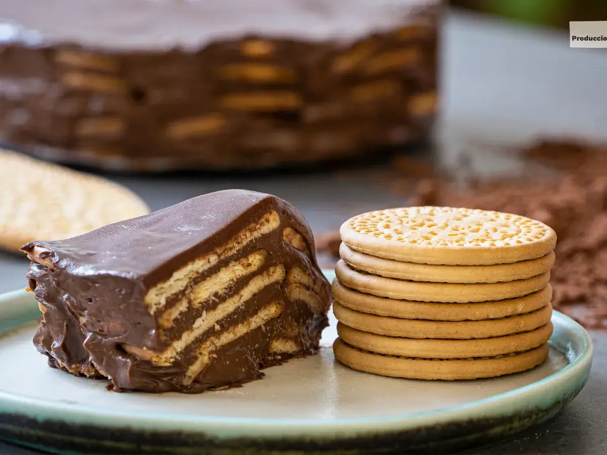 Una porci&oacute;n de marquesa de chocolate, con capas de galletas y crema de cacao, junto a galletas enteras y espolvoreado de cacao.