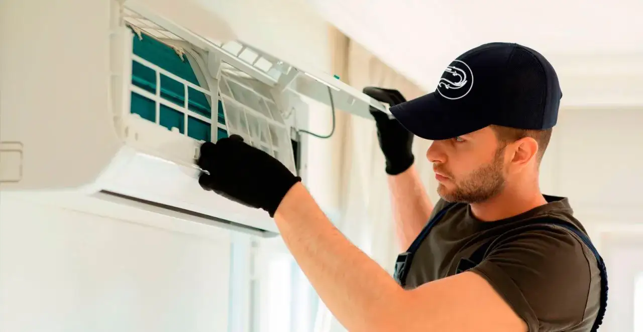 Técnico con guantes negros abre unidad de aire acondicionado para limpiar filtros.