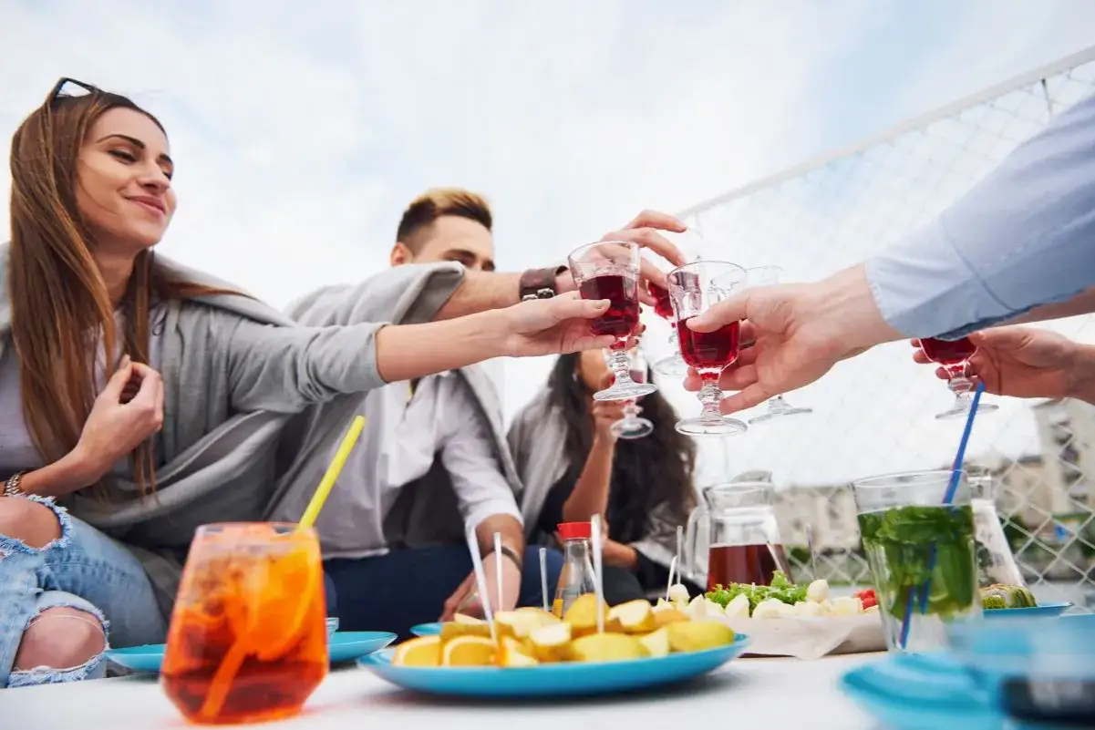 Grupa przyjaciół wznosi kieliszki z czerwonym aperitifem, celebrując radosne spotkanie.