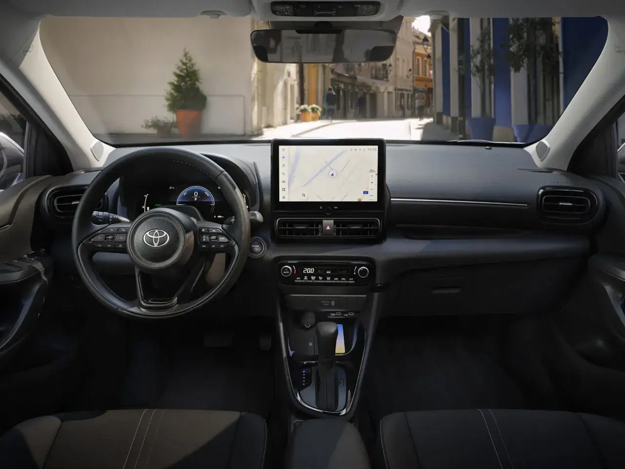 Wnętrze Toyota Yaris Cross Hybrid. Kierownica, ekran multimedialny z nawigacją i widok ulicy za przednią szybą.