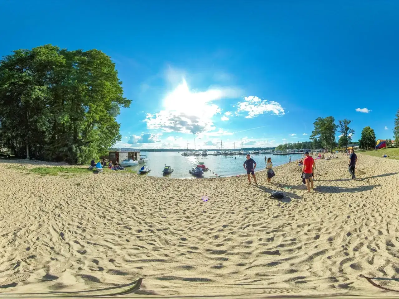 Słoneczny dzień na jednej z najpiękniejszych plaż na Mazurach. Piasek, woda, łodzie i ludzie cieszący się latem.
