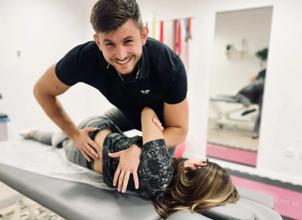 Uśmiechnięty chiropraktyk wykonuje zabieg na pacjentce leżącej na kozetce.