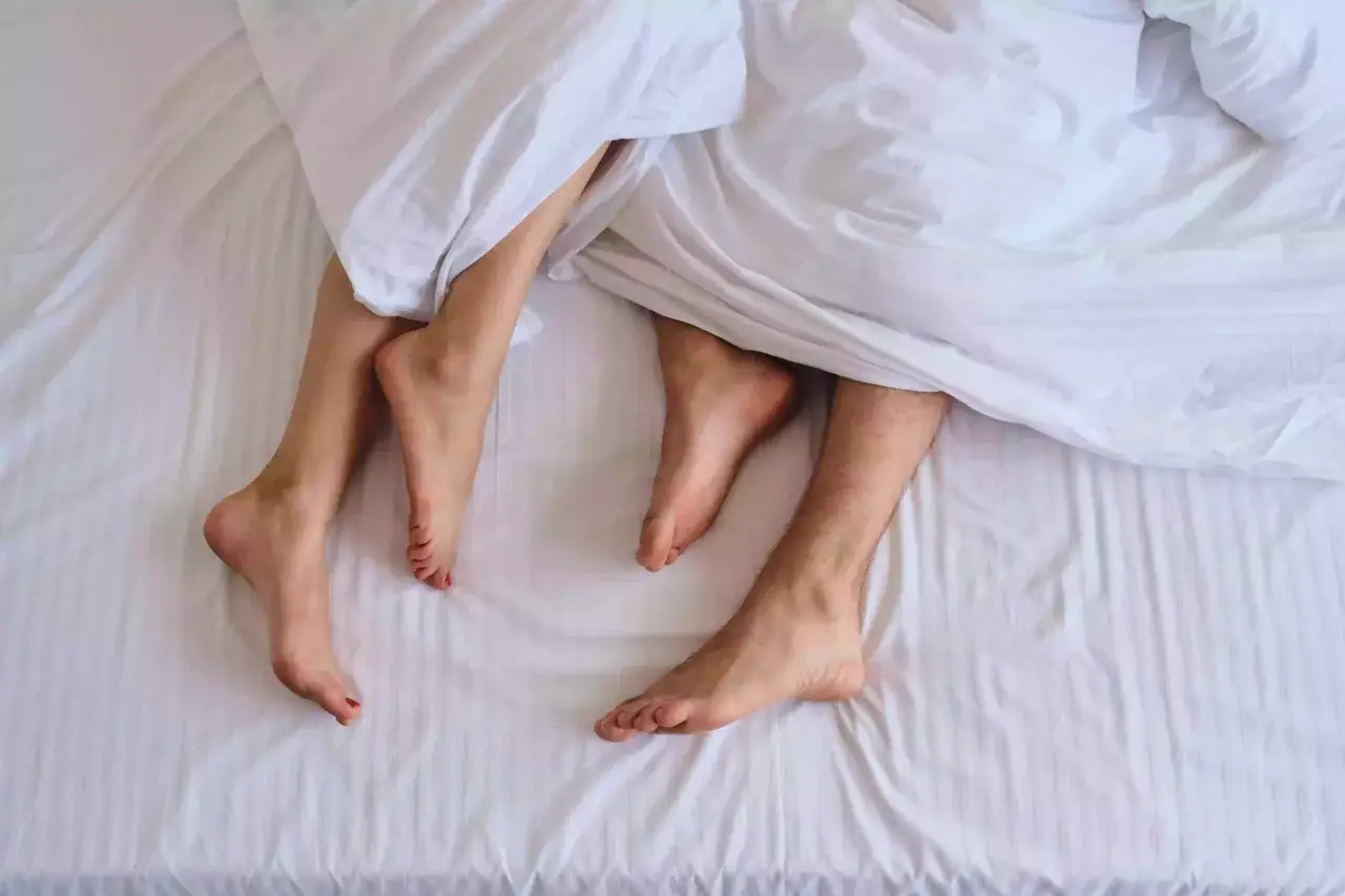 Gambe di uomo e donna sotto le lenzuola bianche, pronte a fare sesso.