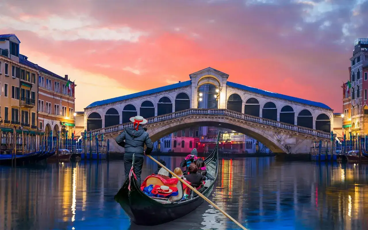 En gondoltur i Venedig vid solnedg&aring;ngen, med Rialtobron i bakgrunden. Undrar du vad kostar det att &aring;ka gondol i Venedig?