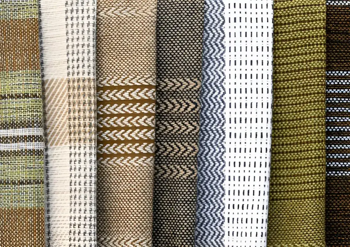 Stoffmuster in verschiedenen Brauntönen, Weiß und Grün. Ein Muster zeigt kleine, unregelmäßige Punkte, was an die Struktur von Tweed erinnert.