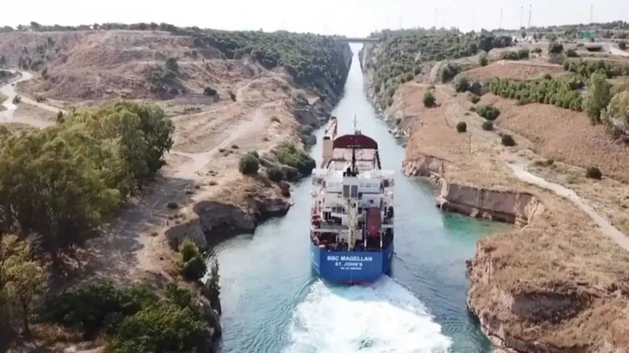 Una nave cargo attraversa il **Canale di Corinto**, navigando tra alte pareti rocciose e vegetazione mediterranea.