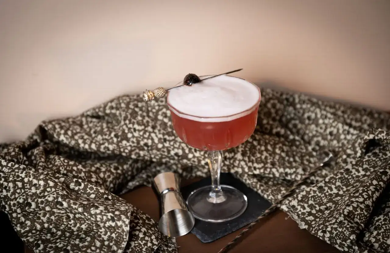 En elegant pink lady drink med skum och k&ouml;rsb&auml;rsgarnityr, redo att avnjutas.