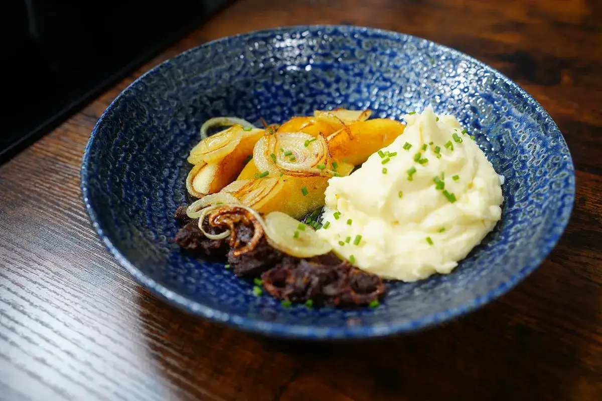 Ein Gericht mit Kartoffelpüree, gebratenen Kartoffelscheiben und Zwiebeln, das an eine harmonische Verbindung von **Himmel und Erde** erinnert.