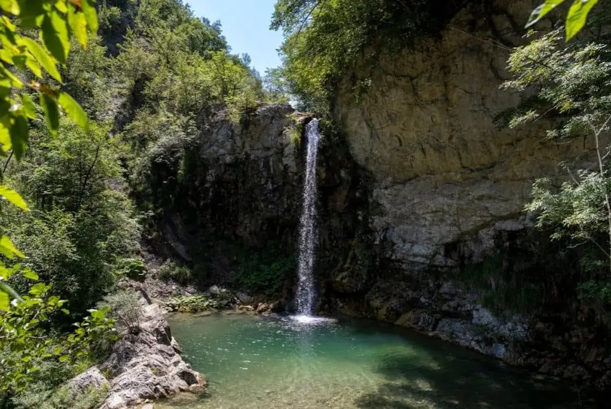 Cascata in una gola rocciosa, un luogo segreto che sembra parte del cammino dei ribelli. L'acqua cristallina scende tra la vegetazione rigogliosa.
