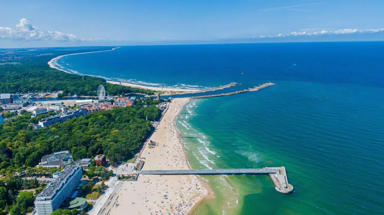 Widok na plażę, morze i molo. W tle las i miasto z diabelskim młynem. Warto zapłacić opłatę klimatyczną za taki wypoczynek.
