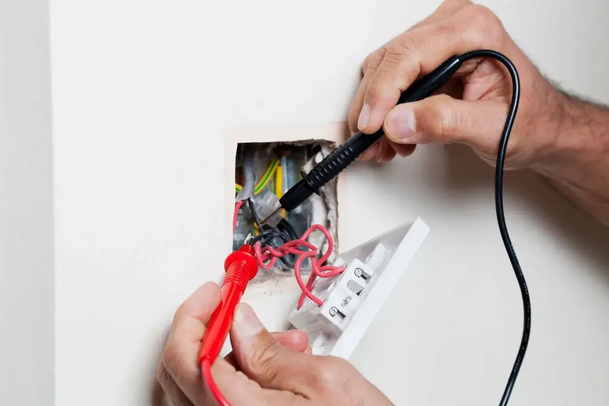 Manos revisando cables con mult&iacute;metro para arreglar el timbre de la puerta.