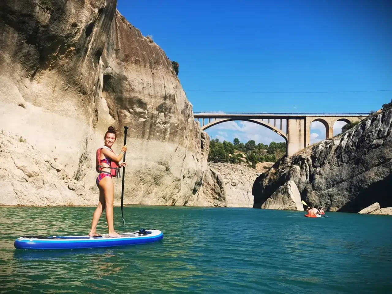 Mujer en paddle surf en una piscina segura de la sierra, con un puente al fondo.