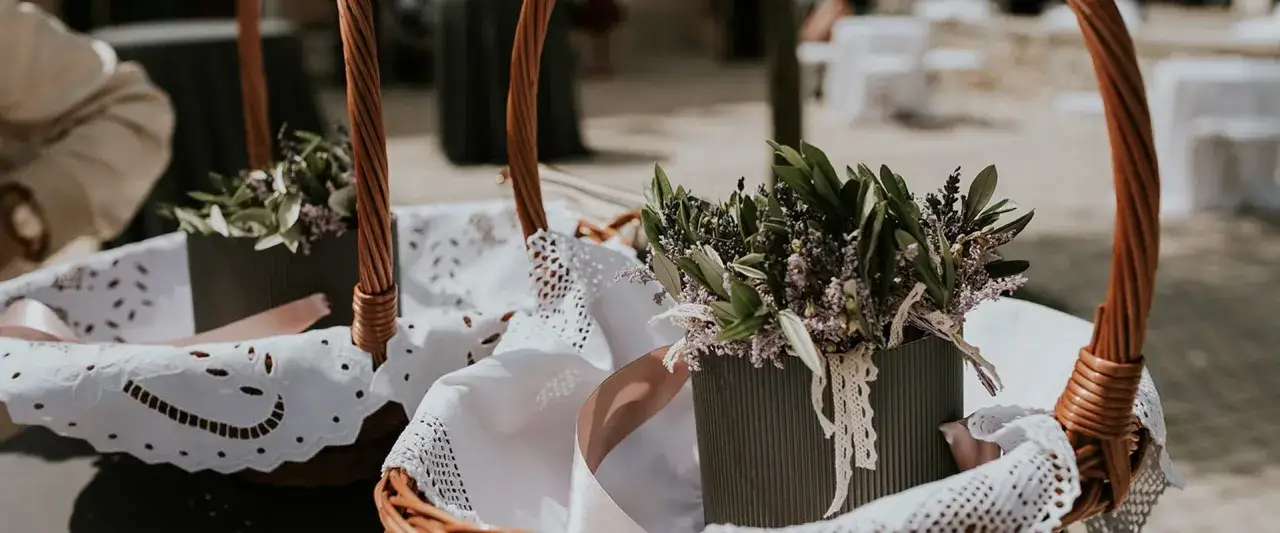 Zwei geflochtene K&ouml;rbe mit Lavendel und Olivenzweigen, bereit f&uuml;r eine kroatische Hochzeit. Wei&szlig;e Spitzendeckchen und rosa B&auml;nder zieren die K&ouml;rbe.