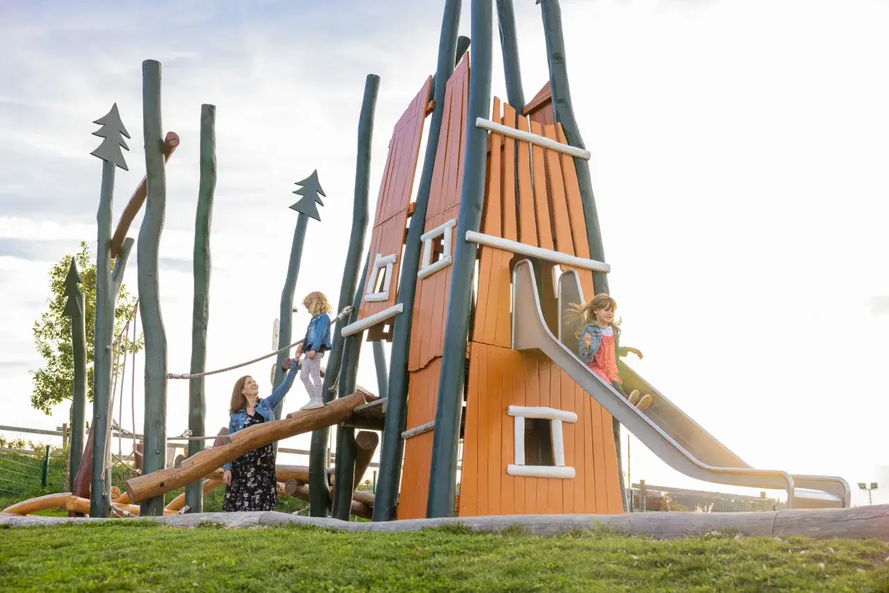 Familie genie&szlig;t einen sonnigen Tag auf einem Abenteuerspielplatz. Kinder klettern und rutschen, w&auml;hrend die Mutter zusieht. Perfekt f&uuml;r Winterberg mit Kindern.