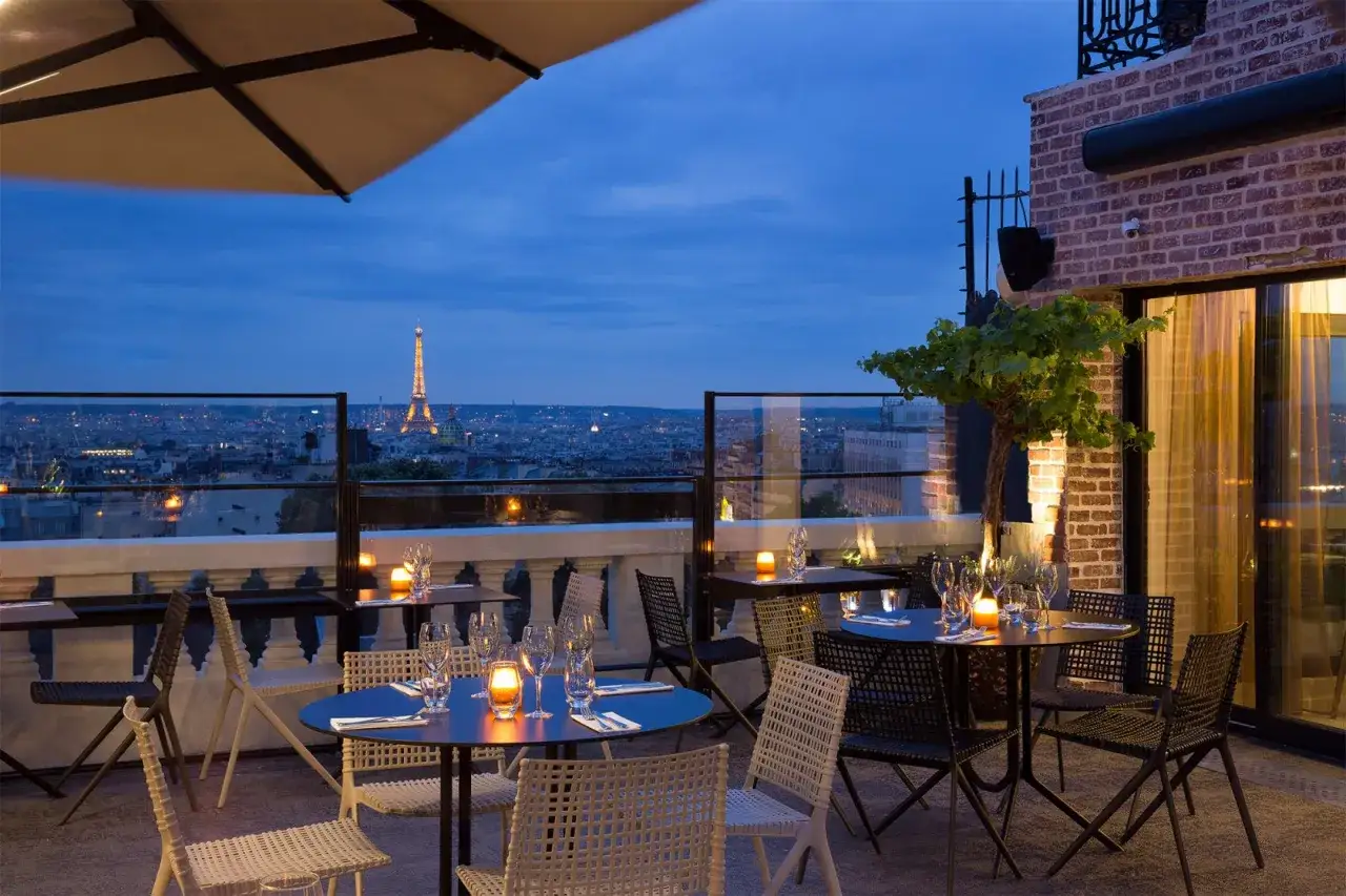 Terrasse d'un restaurant parisien avec vue sur la Tour Eiffel illuminée. Tables dressées pour un dîner romantique, ambiance 
