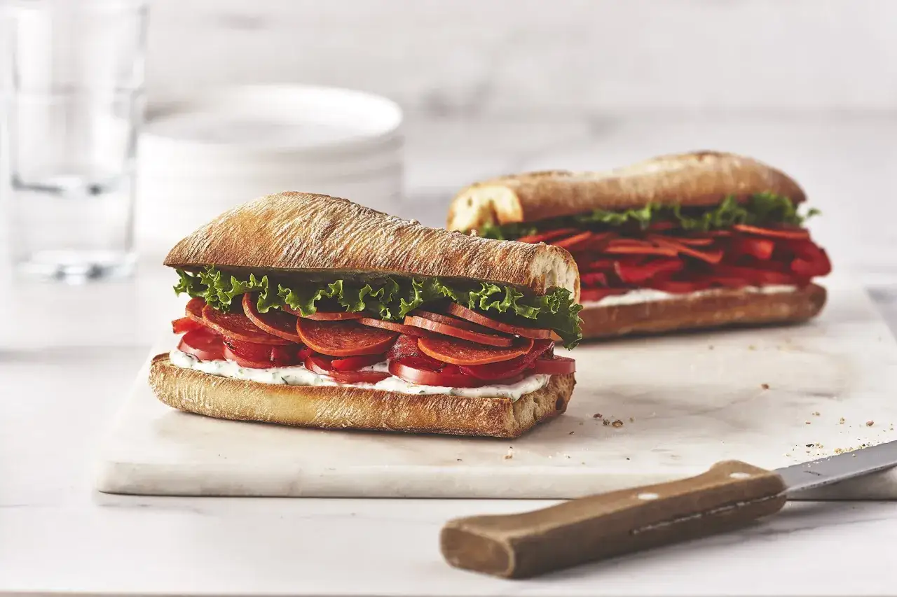 Deux sandwichs appétissants sur pain ciabatta, garnis de pepperoni, tomates, laitue et sauce crémeuse. Une recette de sandwich simple et savoureuse.