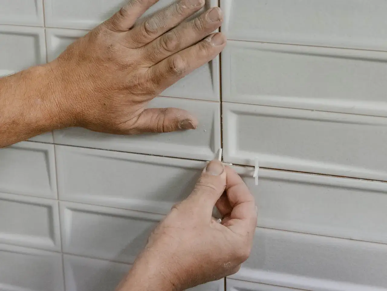 Manos colocando cuñas en las juntas de un azulejo rectificado blanco para asegurar un acabado perfecto.