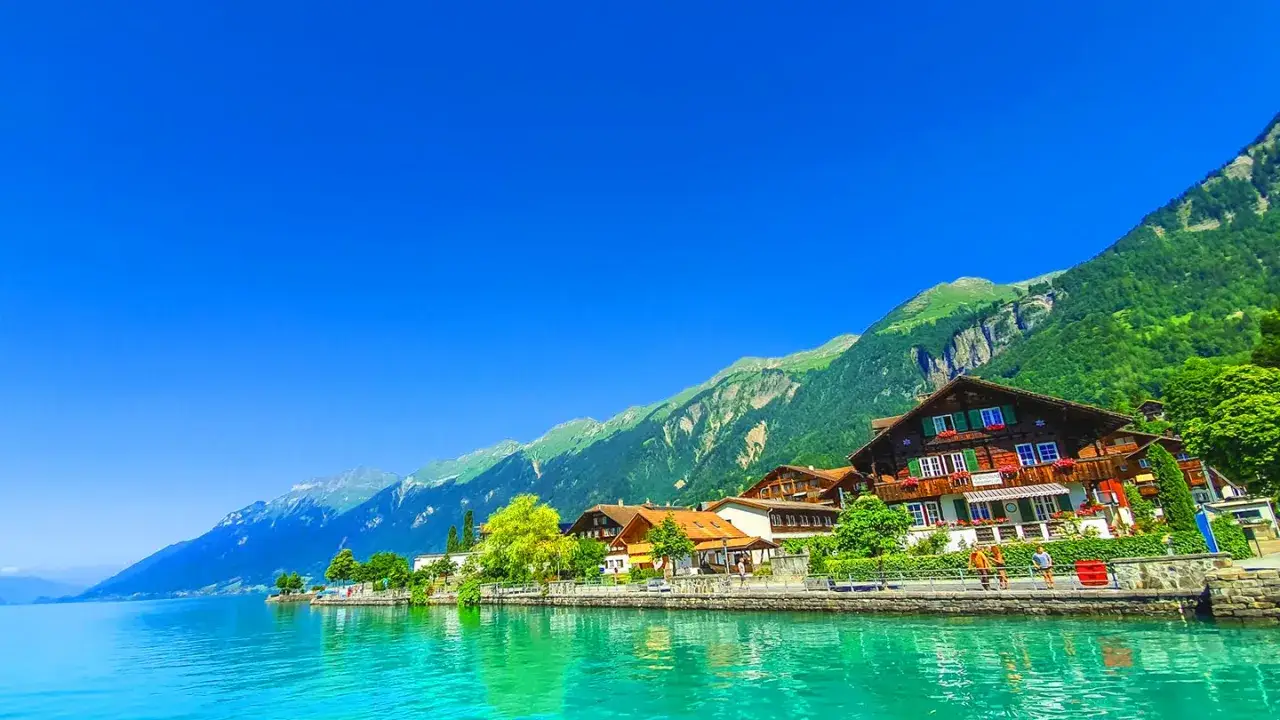 Vackert schweiz resmål vid en turkos sjö med traditionella trähus och gröna berg.