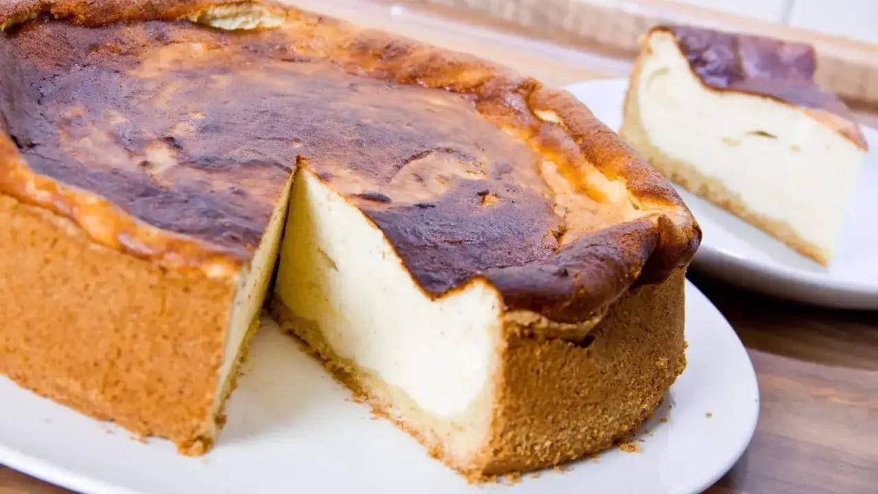 Ein saftiger Quarkkuchen ohne Boden mit karamellisierter Kruste, ein St&uuml;ck davon auf einem Teller.