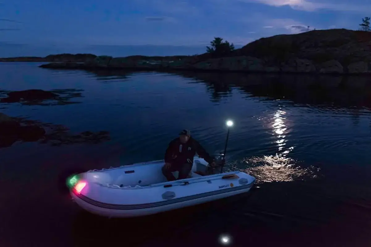 Mann im Schlauchboot bei Nacht. Grüne und rote Lichter am Bug, Mastlicht. Erfüllt die Vorschrift für Schlauchboot Beleuchtung.