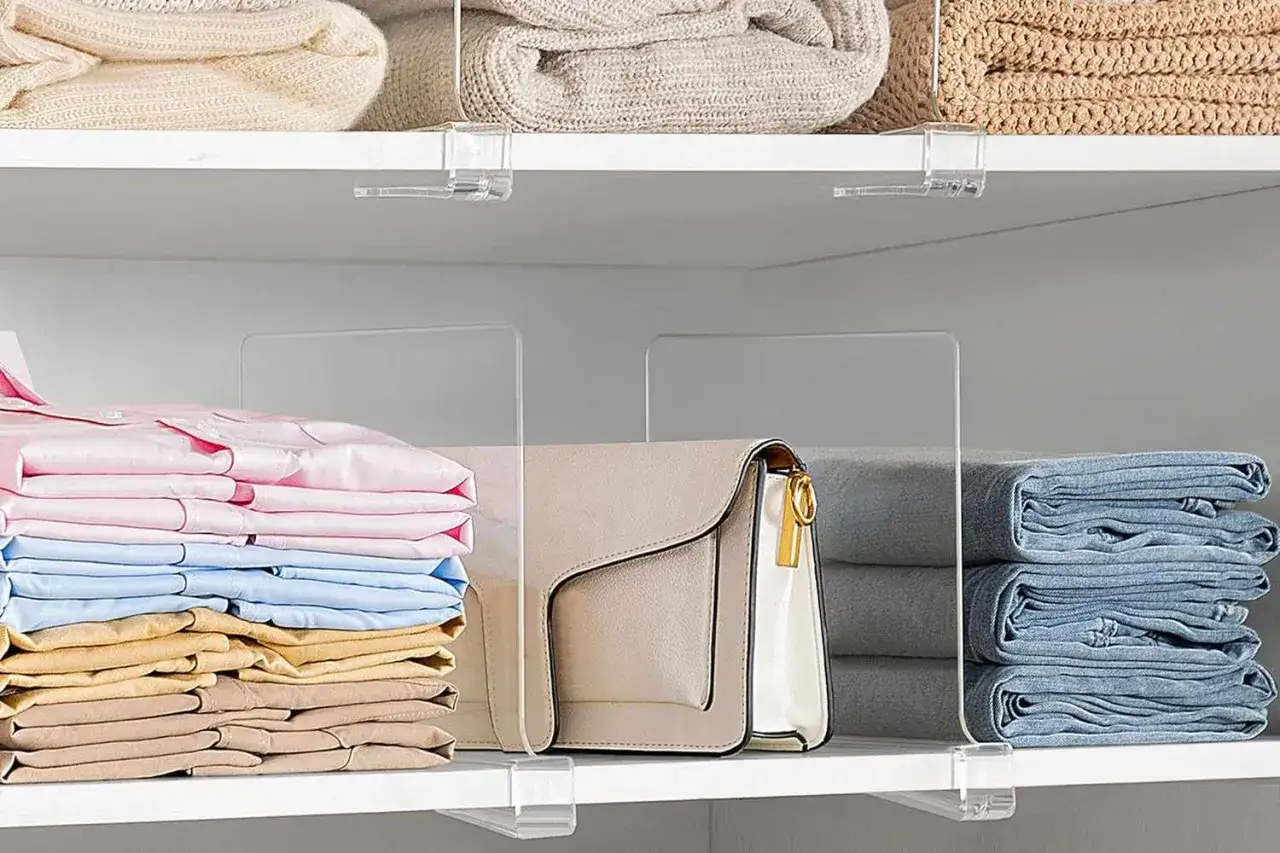 Neatly folded clothes and a handbag are organized on shelves with clear dividers, perfect for a spring cleaning checklist.
