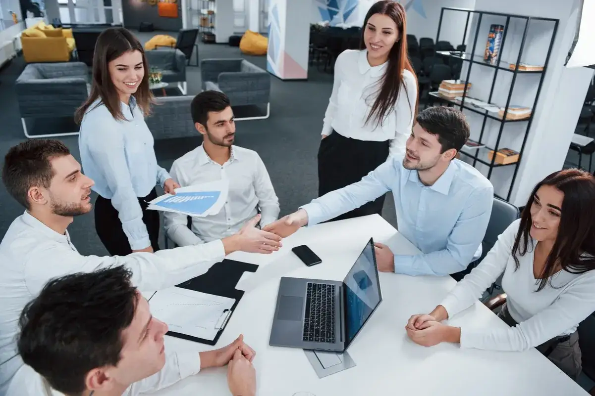 Equipo colaborando en una reuni&oacute;n, discutiendo estrategias de **direcci&oacute;n comercial** con gr&aacute;ficos y un port&aacute;til.