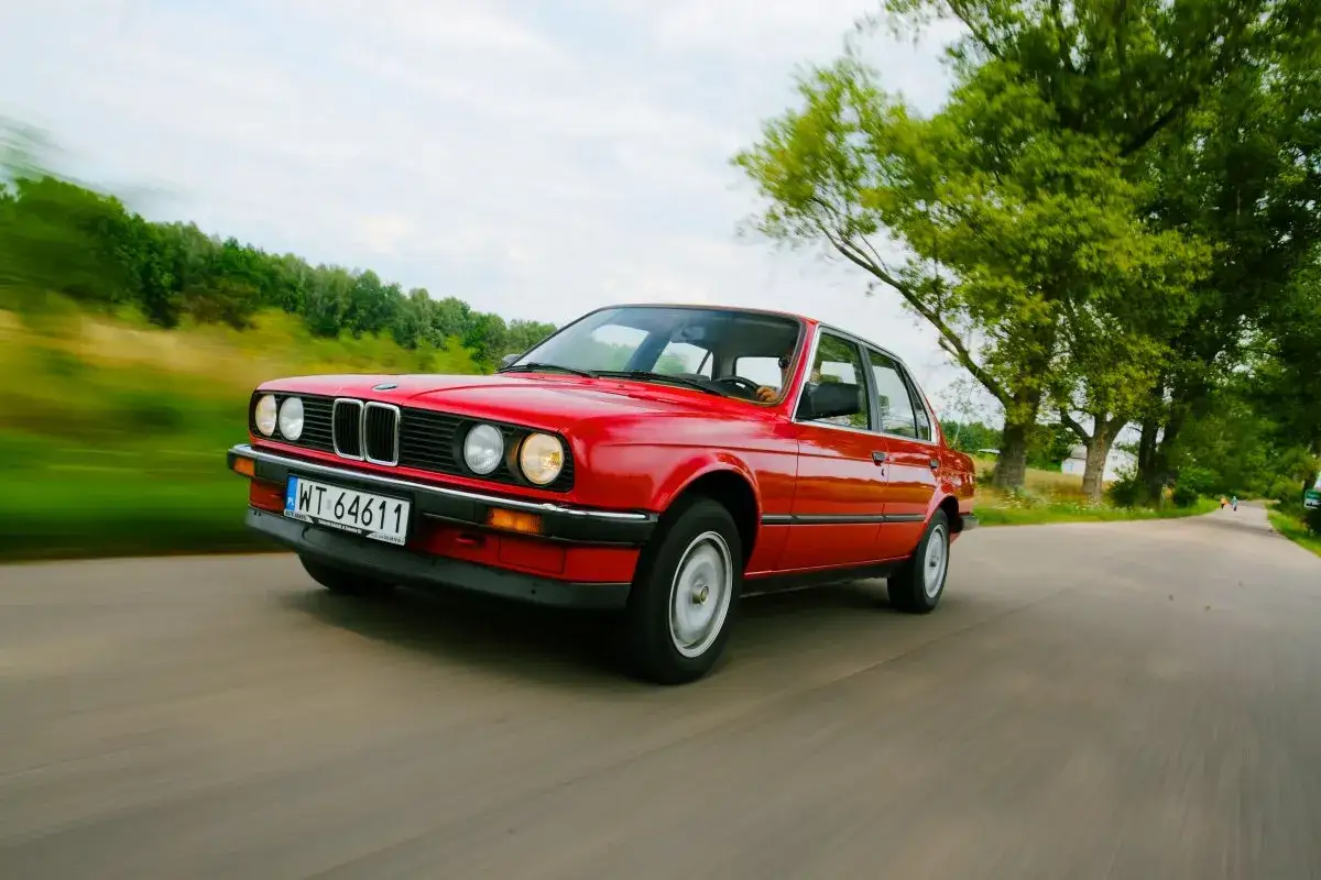 Czerwone bmw e30 coupe pędzi wiejską drogą wśród zieleni.