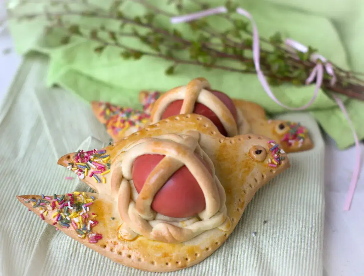 Scarcelle pugliesi ricetta originale: dolci a forma di colomba con uova rosse e codine colorate, pronti per la Pasqua.