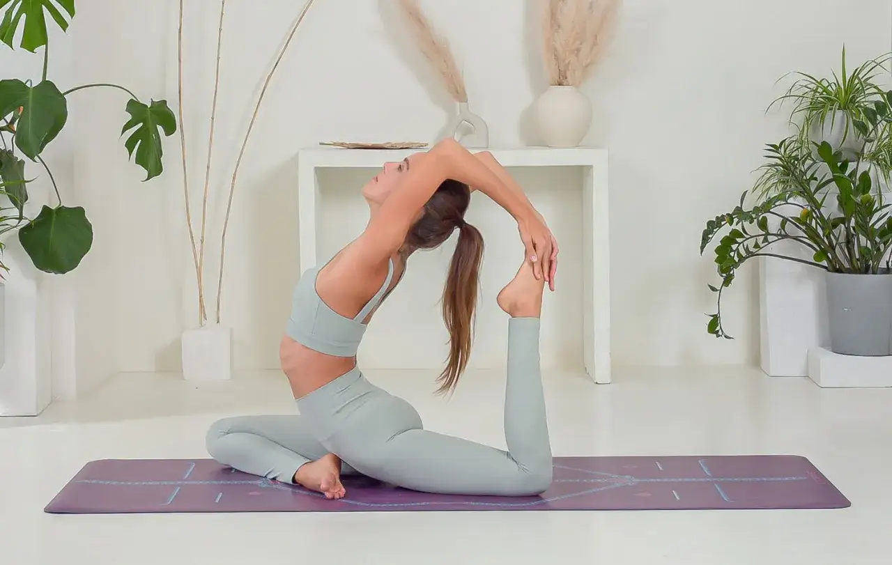 Kobieta w pozycji kapotasana na macie do jogi, zgięta w łuk, chwyta stopę.