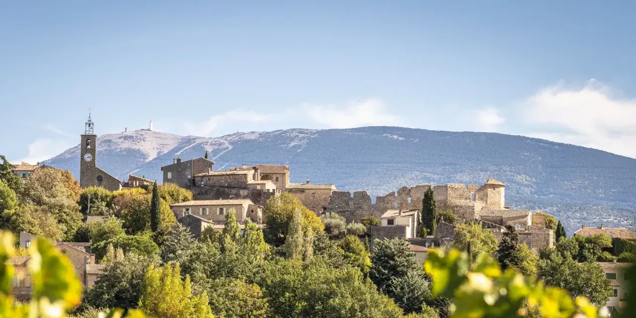Vue d'un faucon village perch&eacute; sur une colline, avec une &eacute;glise et des ruines de ch&acirc;teau. Le Mont Ventoux domine l'horizon.
