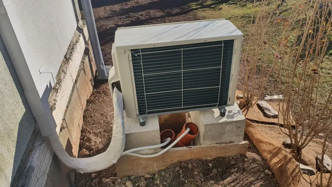 Au&szlig;enunit einer Klimaanlage zum Heizen, montiert auf Betonbl&ouml;cken neben einem Haus.