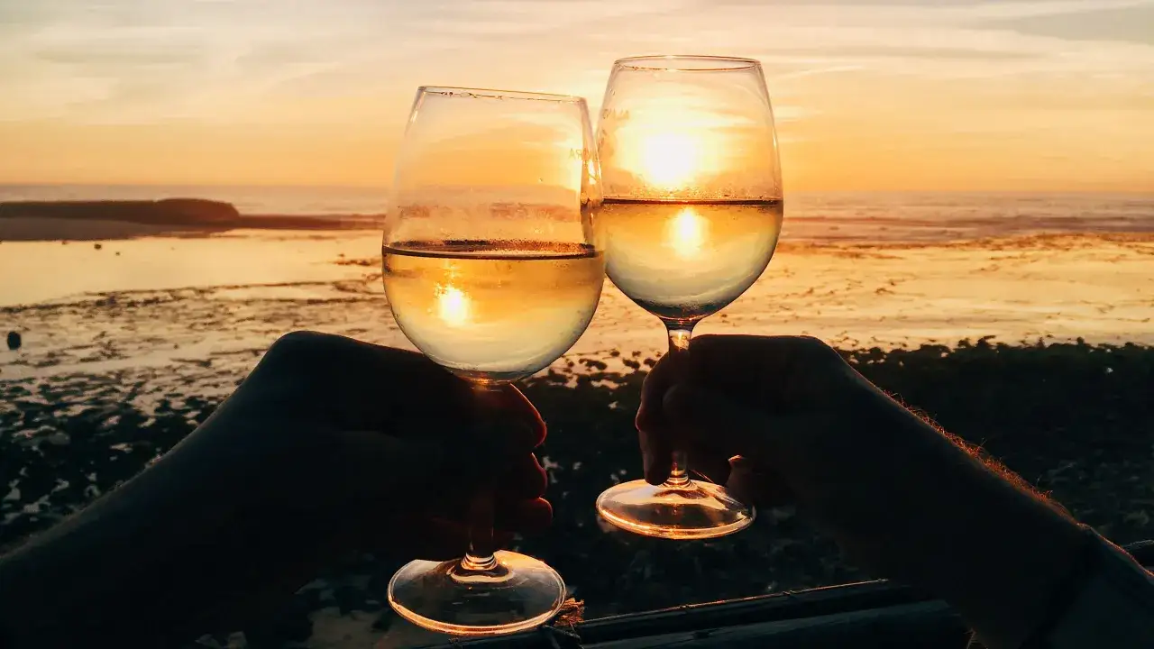 Due calici di ribolla gialla brillano al tramonto sulla spiaggia.