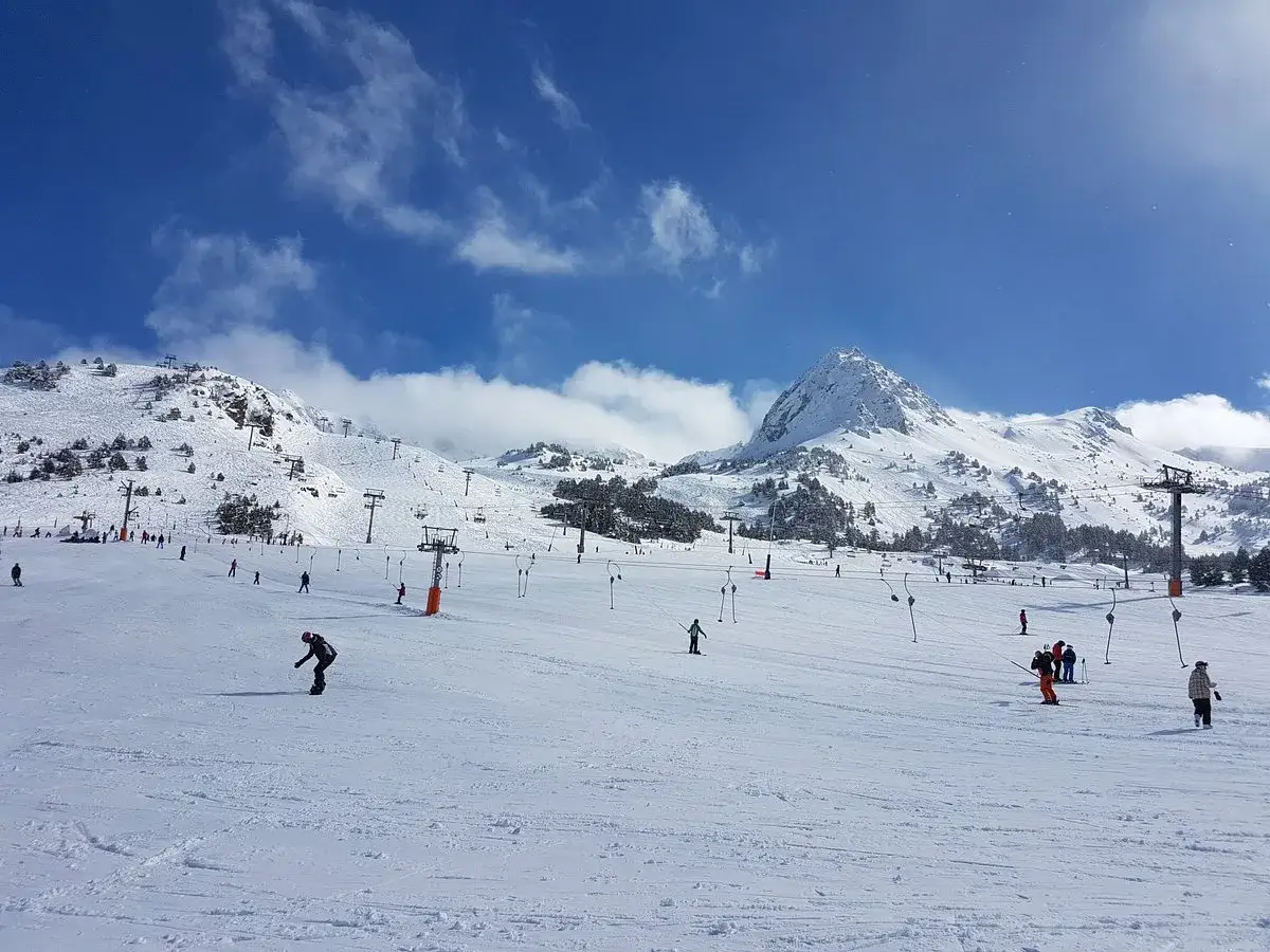 Esqu&iacute; en Grau Roig, con pistas nevadas, telesillas y un pico monta&ntilde;oso imponente bajo un cielo azul con nubes.