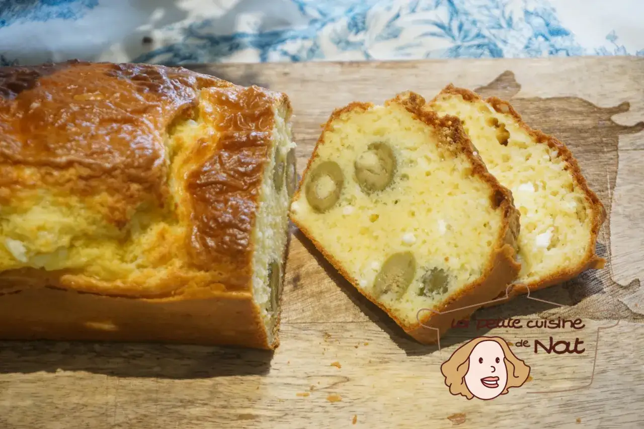 Savoureux cake salé aux olives et feta, doré et moelleux, coupé en tranches sur une planche en bois.