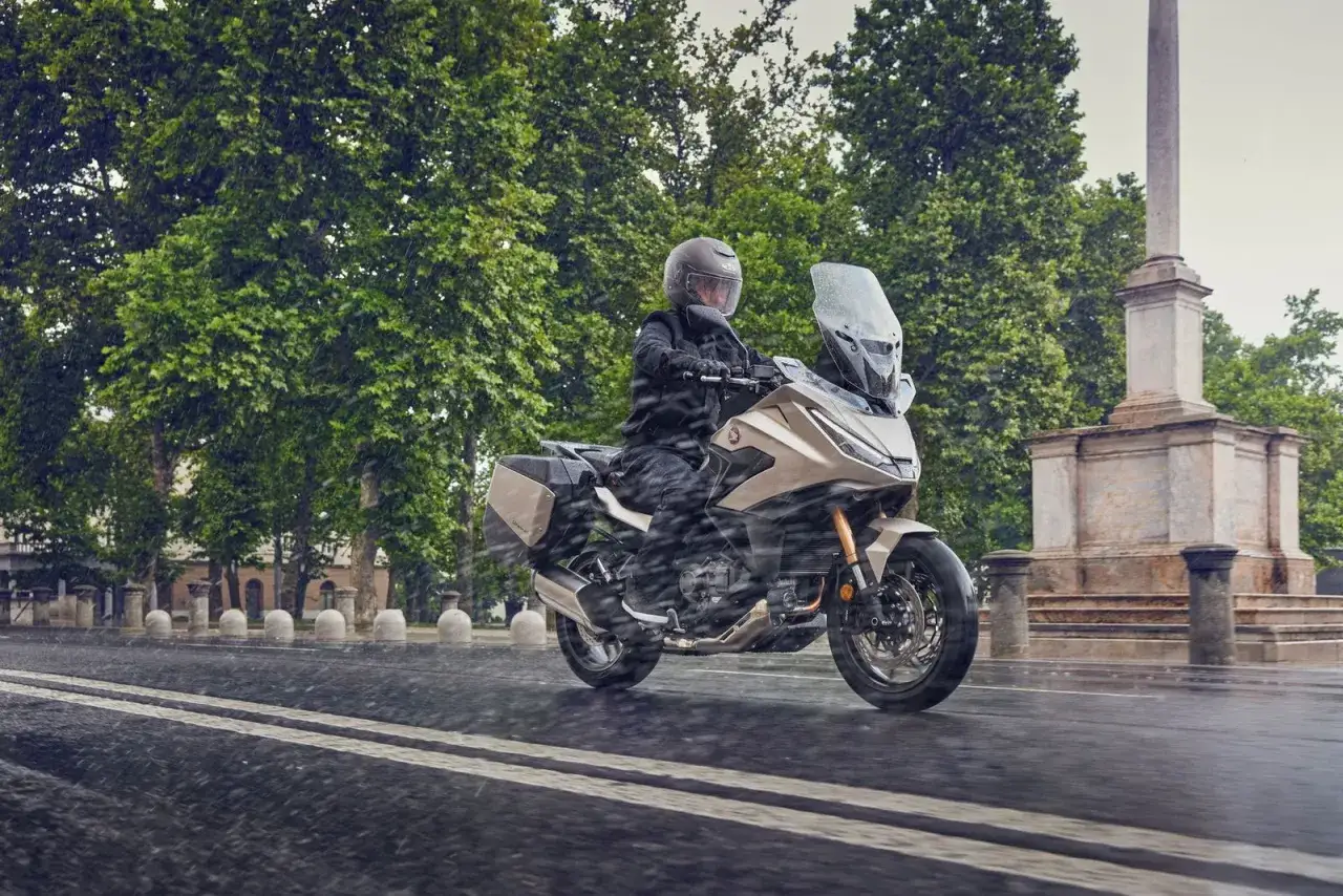 Motociclista con casco y chaqueta negra conduce una Honda NT 1100 color beige bajo la lluvia. Las opiniones sobre esta moto son muy positivas.