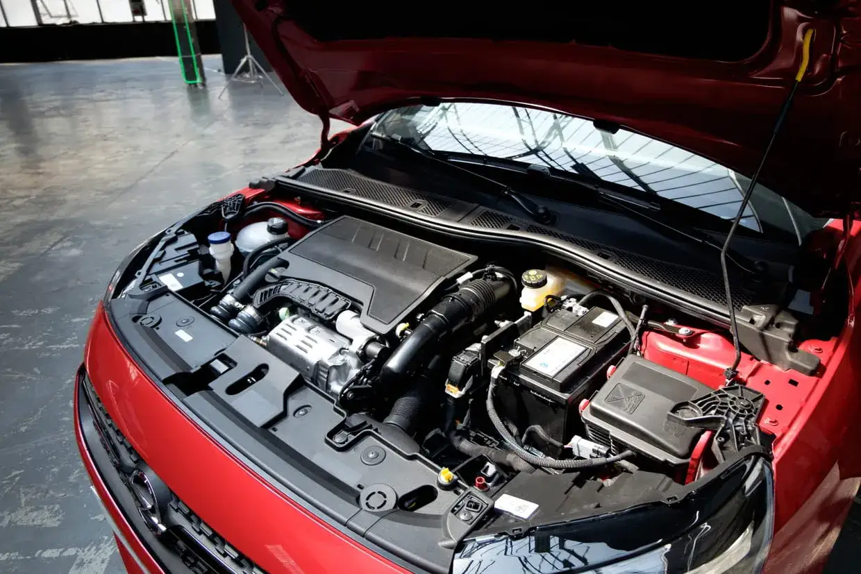 Le capot ouvert révèle le moteur d'une Opel Corsa rouge, avec sa batterie et ses composants bien visibles.