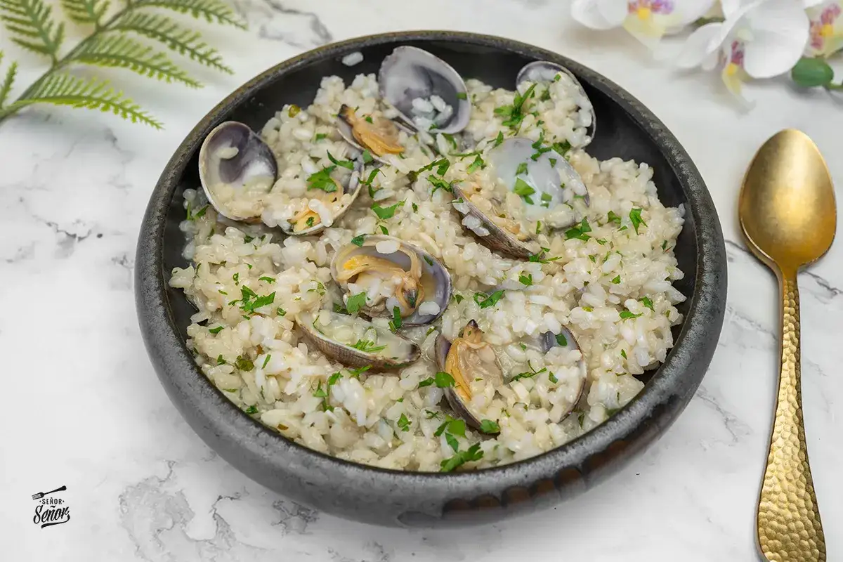 Un cremoso arroz con almejas, adornado con perejil fresco, servido en un cuenco oscuro.