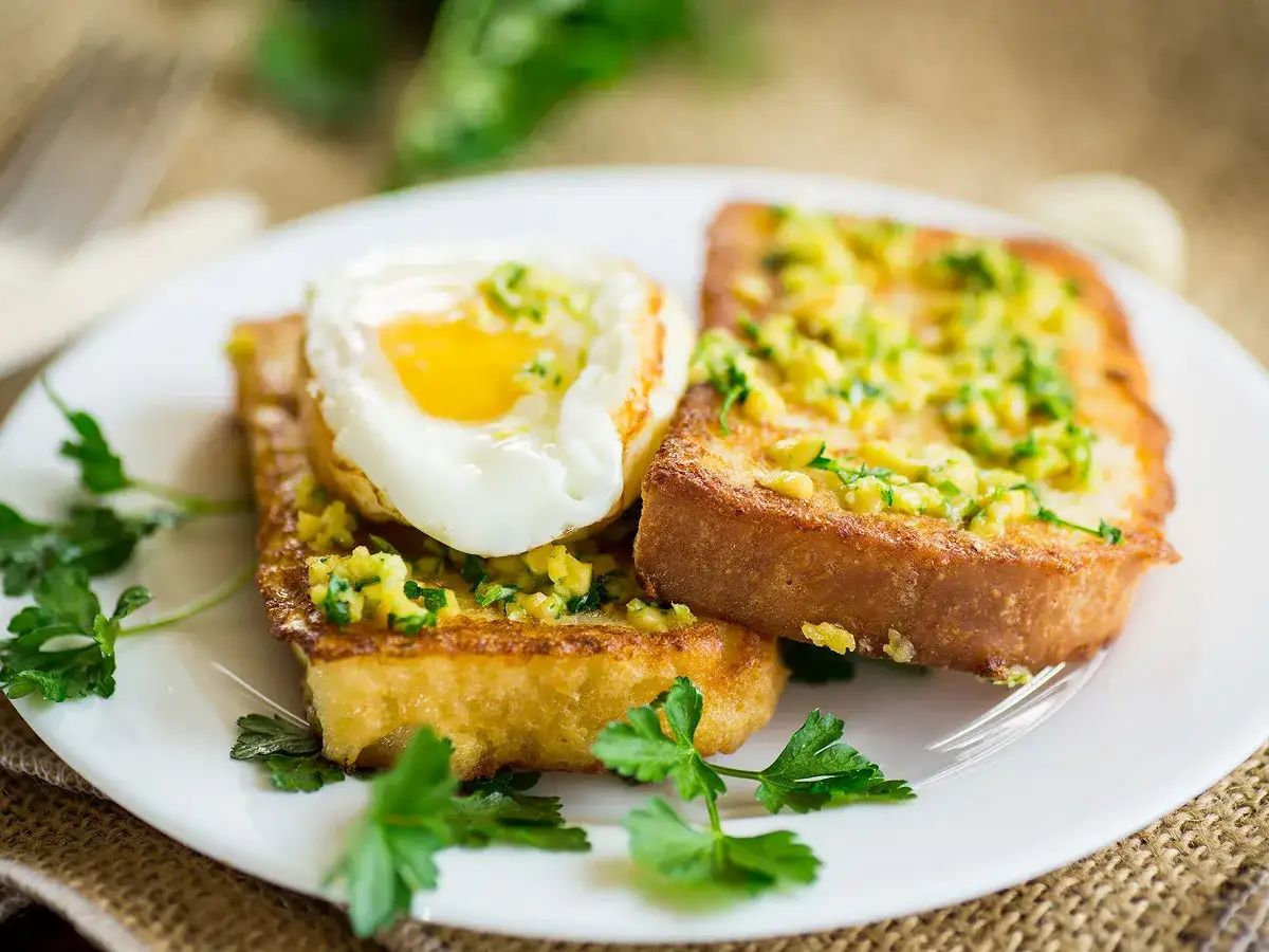 Pain perdu salé garni d'un œuf au plat et d'herbes fraîches, servi sur une assiette blanche.