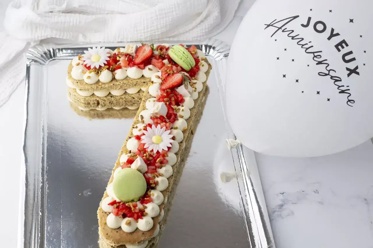 Un d&eacute;licieux number cake pistache, garni de fraises, macarons et fleurs en sucre, pr&ecirc;t pour un joyeux anniversaire.