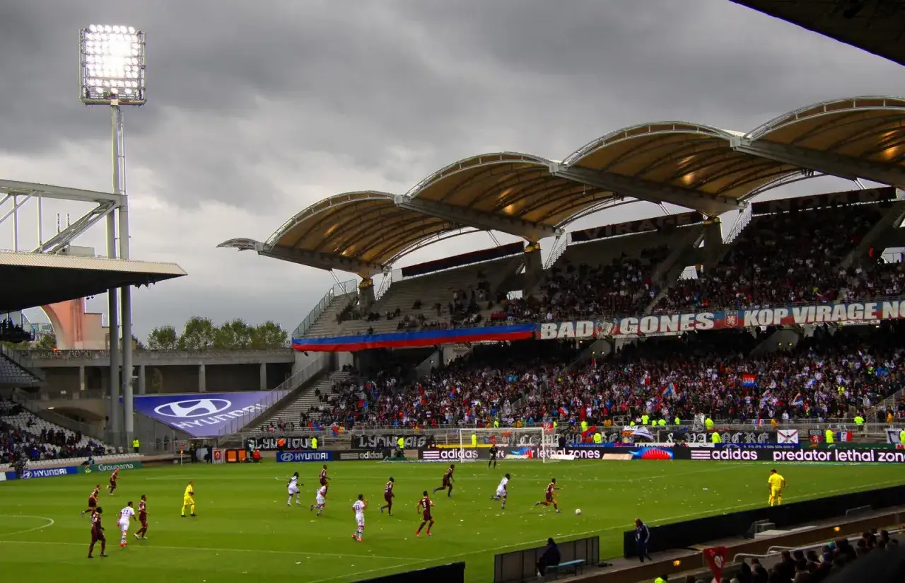 Mecz na stadionie klubu Lyon. Tłumy kibiców na trybunach, piłkarze na murawie.
