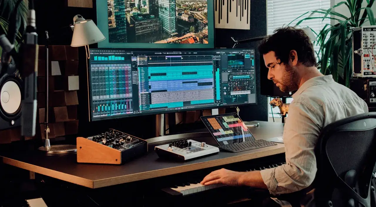 Un homme crée un son dans son studio, manipulant des pistes sur un écran large et jouant d'un clavier.