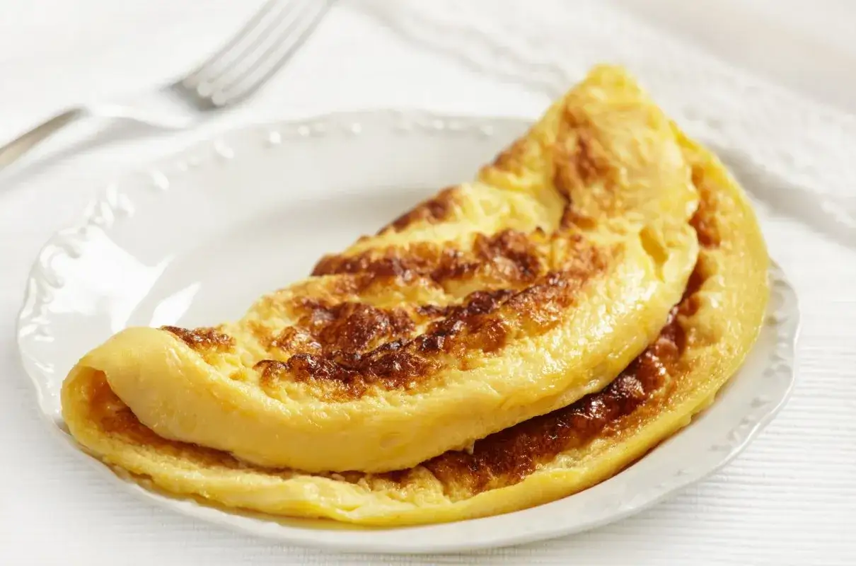 Złocisty omlet z bananem, złożony na pół, na białym talerzu. Idealny na słodkie śniadanie.