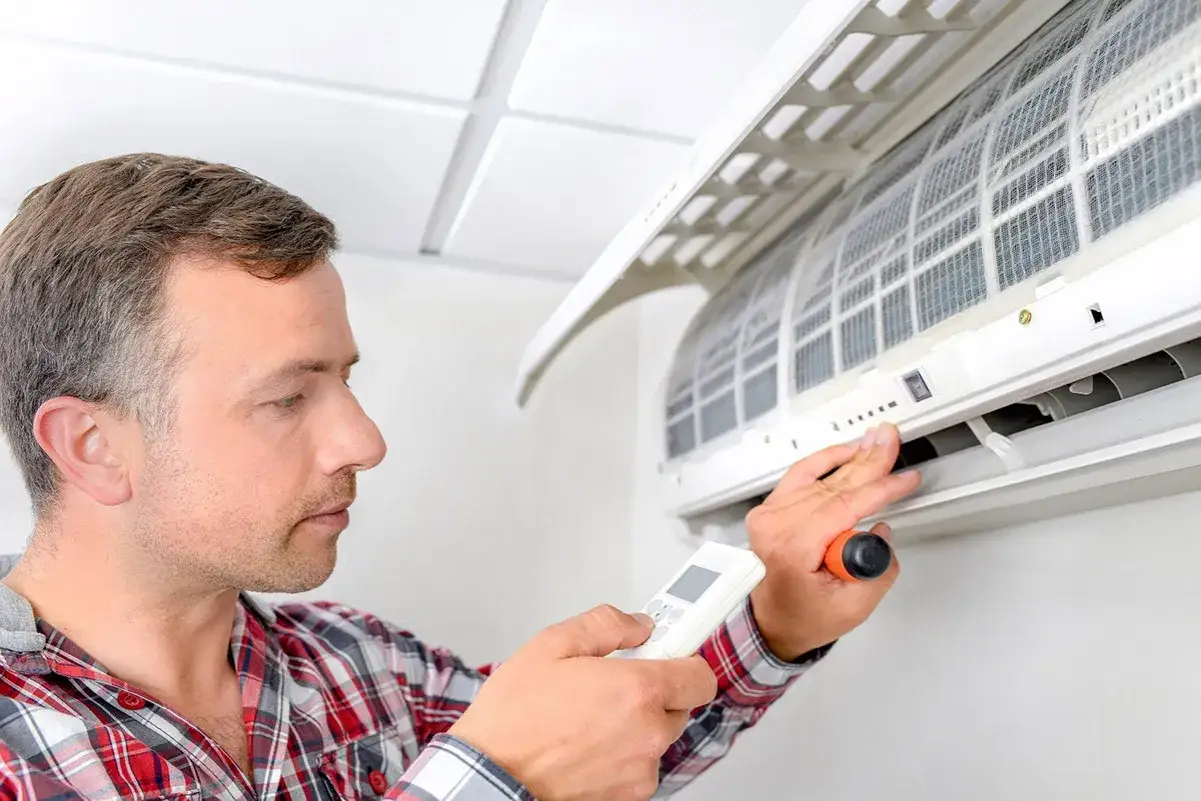 Mężczyzna z pilotem i śrubokrętem przy jednostce klimatyzacyjnej. Dowiedz się, jak zamontować klimatyzację.
