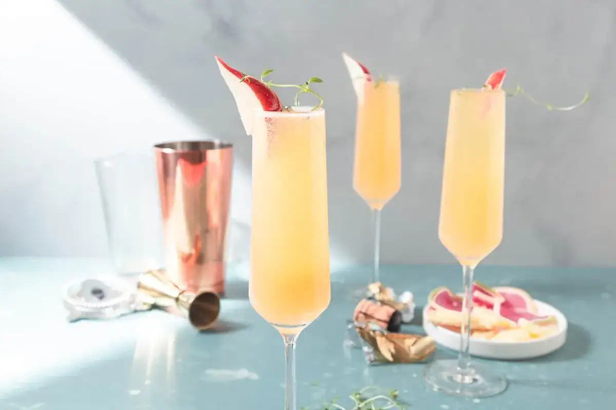 Tre eleganta glas med drinkar med gin och prosecco, garnerade med tunna äppelskivor och örter. En kopparskakare och mätkopp syns i bakgrunden.
