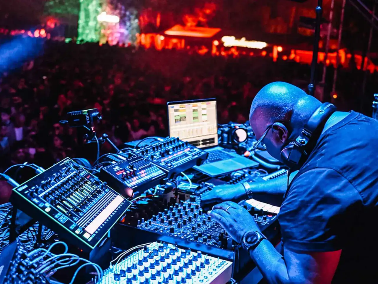 DJ con cuffie mixa musica elettronica, creando le sue canzoni. La folla balla sotto luci colorate.