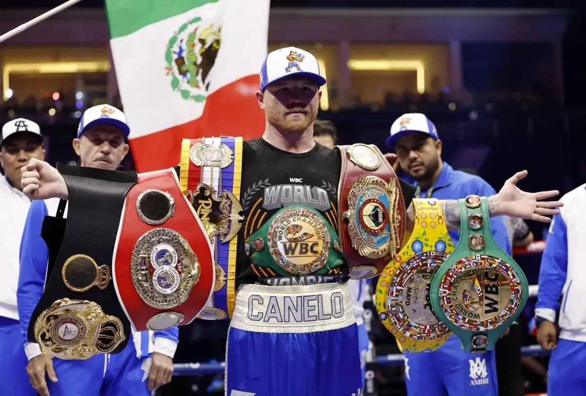 Canelo Alvarez proudly displays his multiple championship belts, a testament to his incredible boxing accomplishments, with the Mexican flag waving behind him.