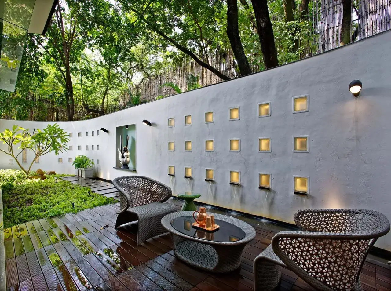 Un patio moderno con muebles de mimbre, un estanque y una pared con nichos iluminados y cascadas, ideal para decorar pared patio exterior.