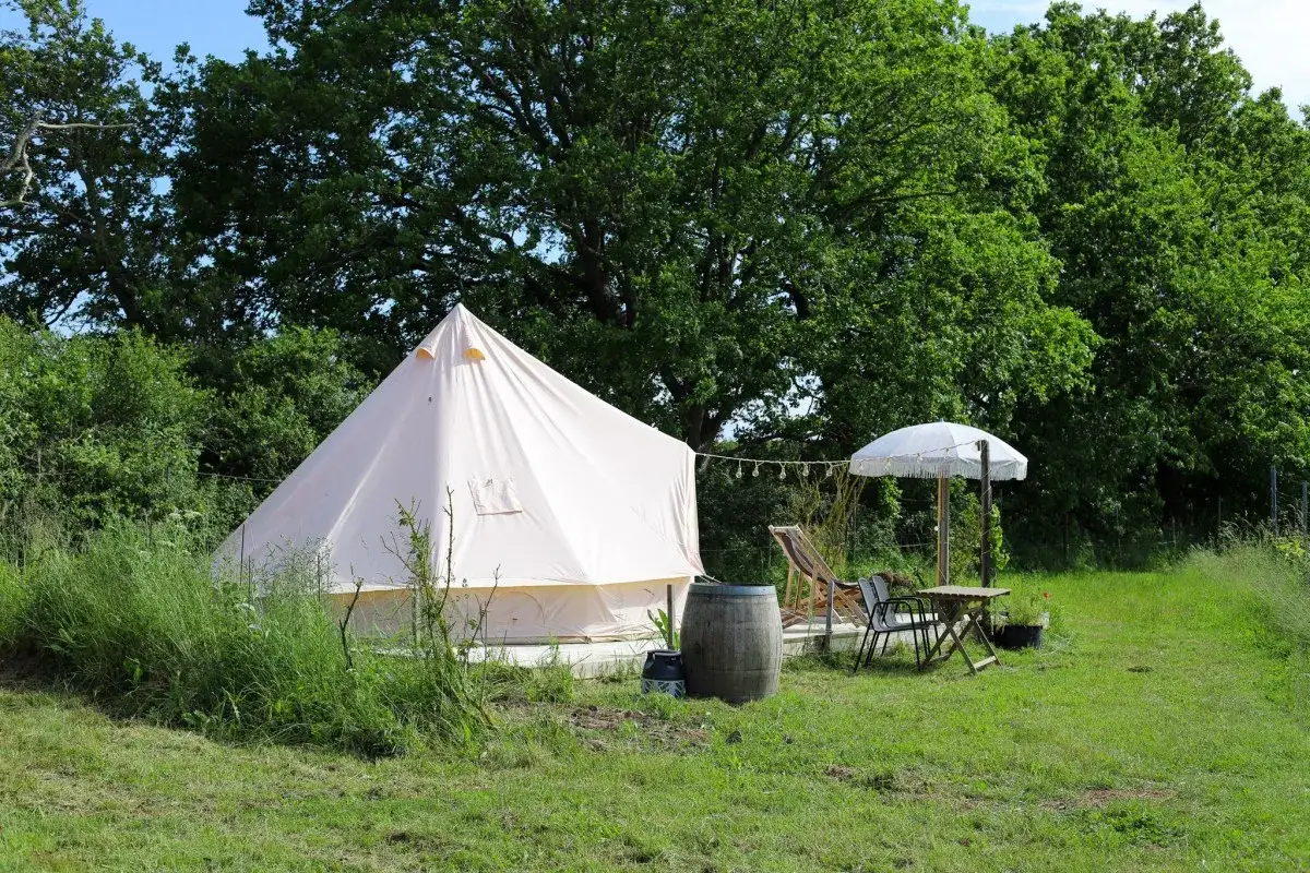 En ljus tipi-tält för glamping i Mölle, med solstol, parasoll och ett litet bord i en grönskande miljö.