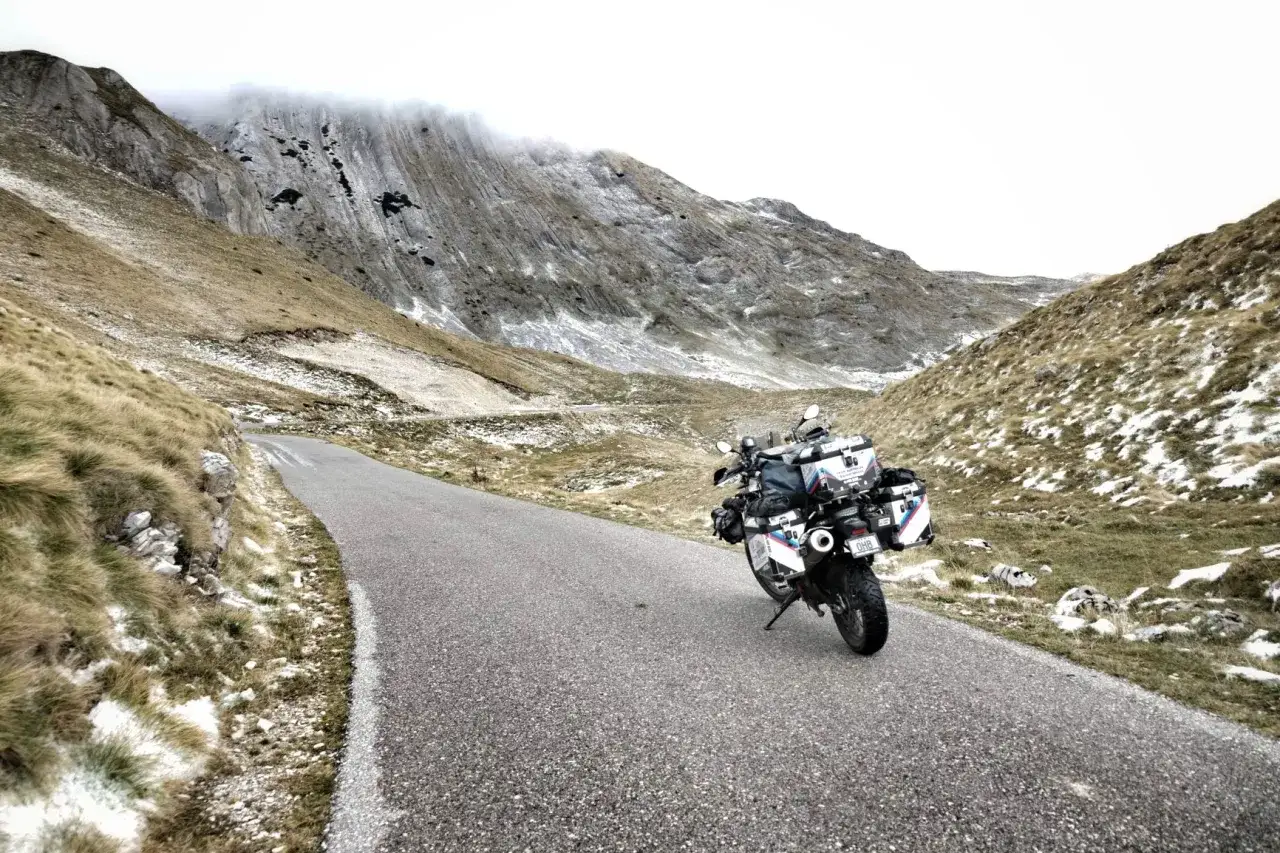 Motocykl zaparkowany na krętej drodze w górach Czarnogóry. W tle skaliste zbocza z resztkami śniegu.