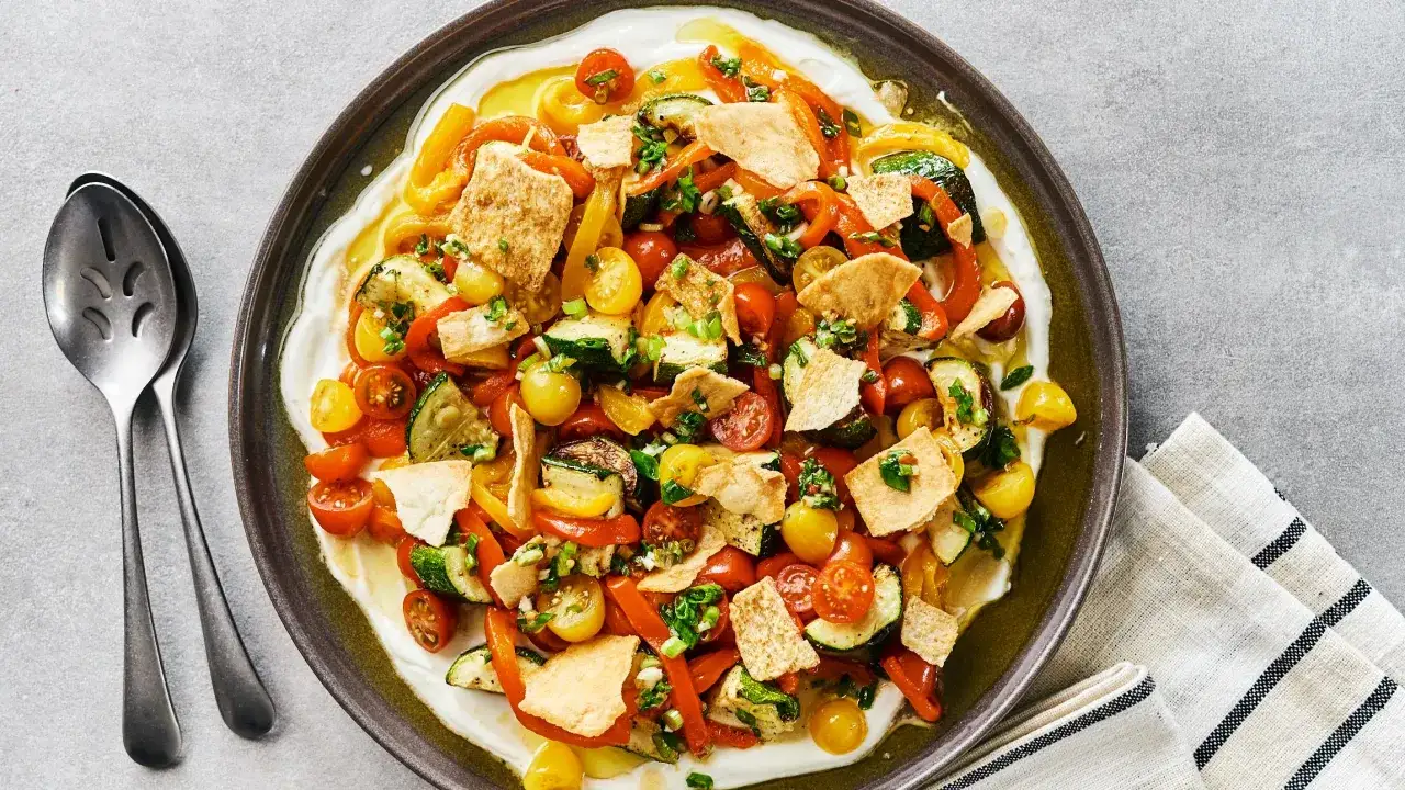 Salade colorée de poivrons grillés, courgettes, tomates cerises et pain pita croustillant, servie sur une base crémeuse.